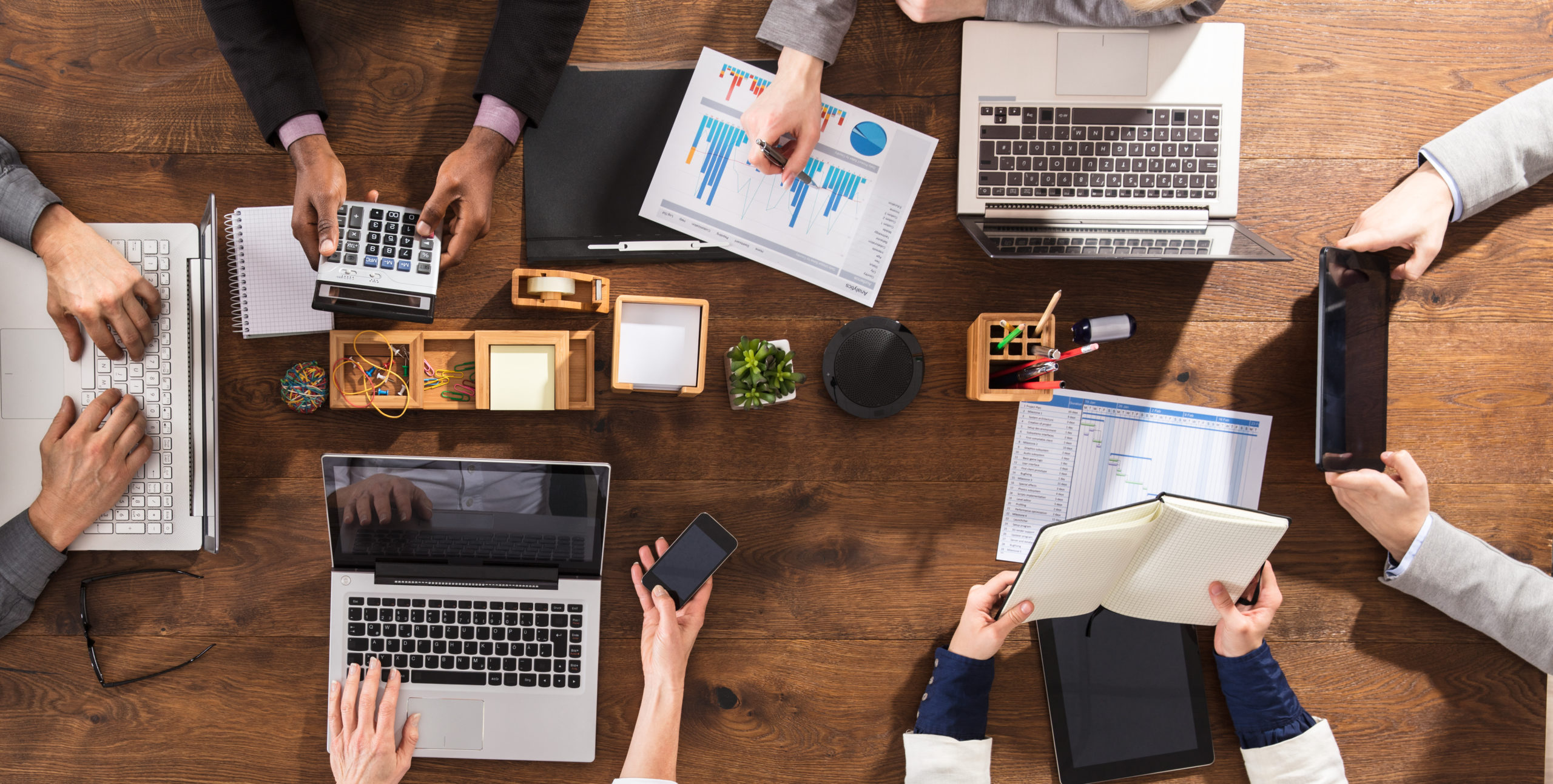 overhead view of businesspeople at a table with laptops, evaluating business data.